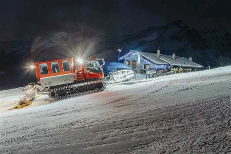 Un gatto delle nevi al lavoro su una pista innevata di notte