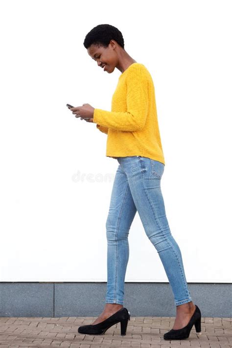 Donna che cammina con cellulare, tuta chiara, capelli sciolti, scale e muro di cemento sullo sfondo