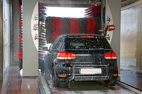 Un'auto che passa attraverso un autolavaggio, con spazzole e getti d'acqua che puliscono le ruote.