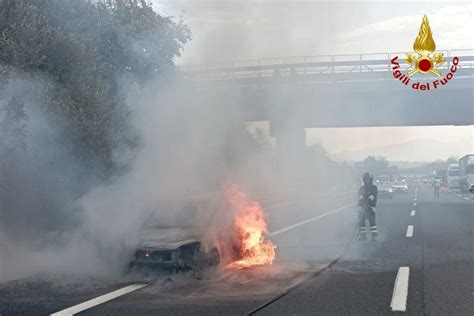 Automobile in fiamme sul ciglio di un'autostrada con i vigili del fuoco che intervengono