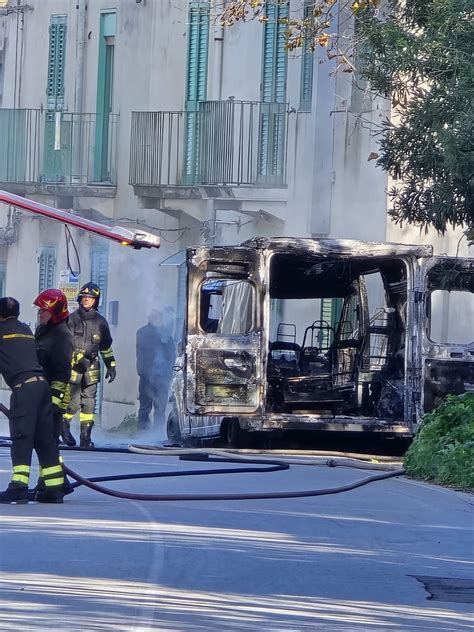 Un'auto distrutta dalle fiamme, con un'ambulanza sullo sfondo